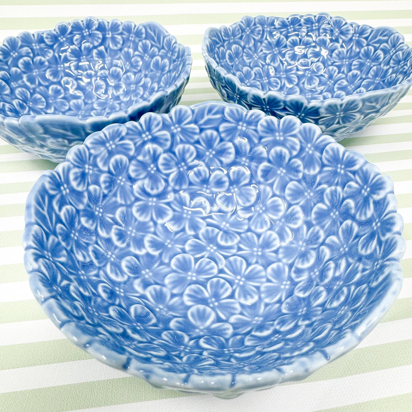 Three light blue ceramic bowls with a floral embossed design. Each bowl features a textured surface covered in small, raised flower shapes creating a three-dimensional effect. The bowls are shallow and have a scalloped edge. These decorative bowls are perfect for serving snacks or candies.