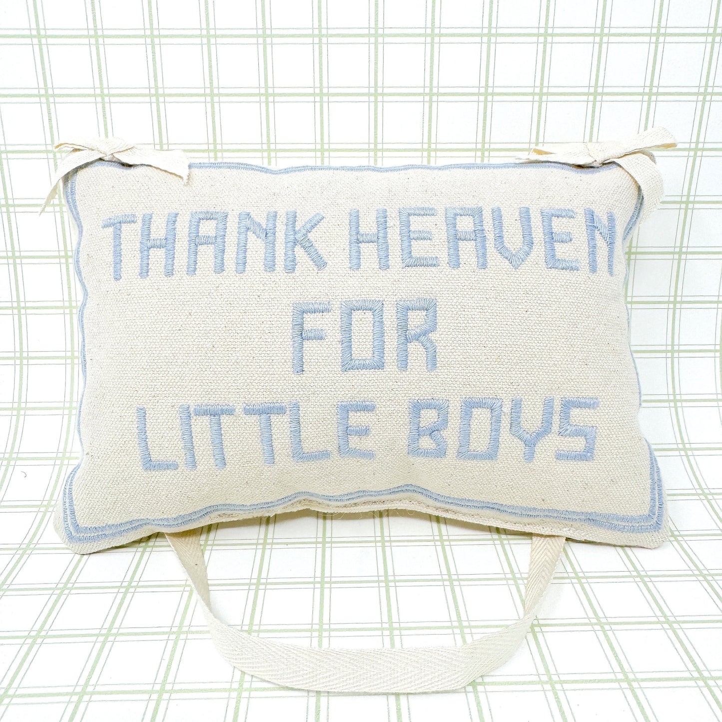 A rectangular white pillow with blue embroidery reading "Thank Heaven For Little Boys," featuring a matching white ribbon loop for hanging, displayed against a plain white background