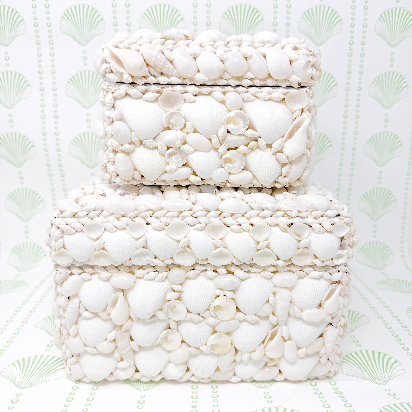 Two white square boxes made of seashells. The boxes are stacked on top of each other. The boxes are made of small white seashells that are arranged in a pattern. The boxes are a decorative storage solution.